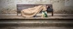 Una persona sin hogar descansa en un banco de madera | Fotografía: Marga Ferrer